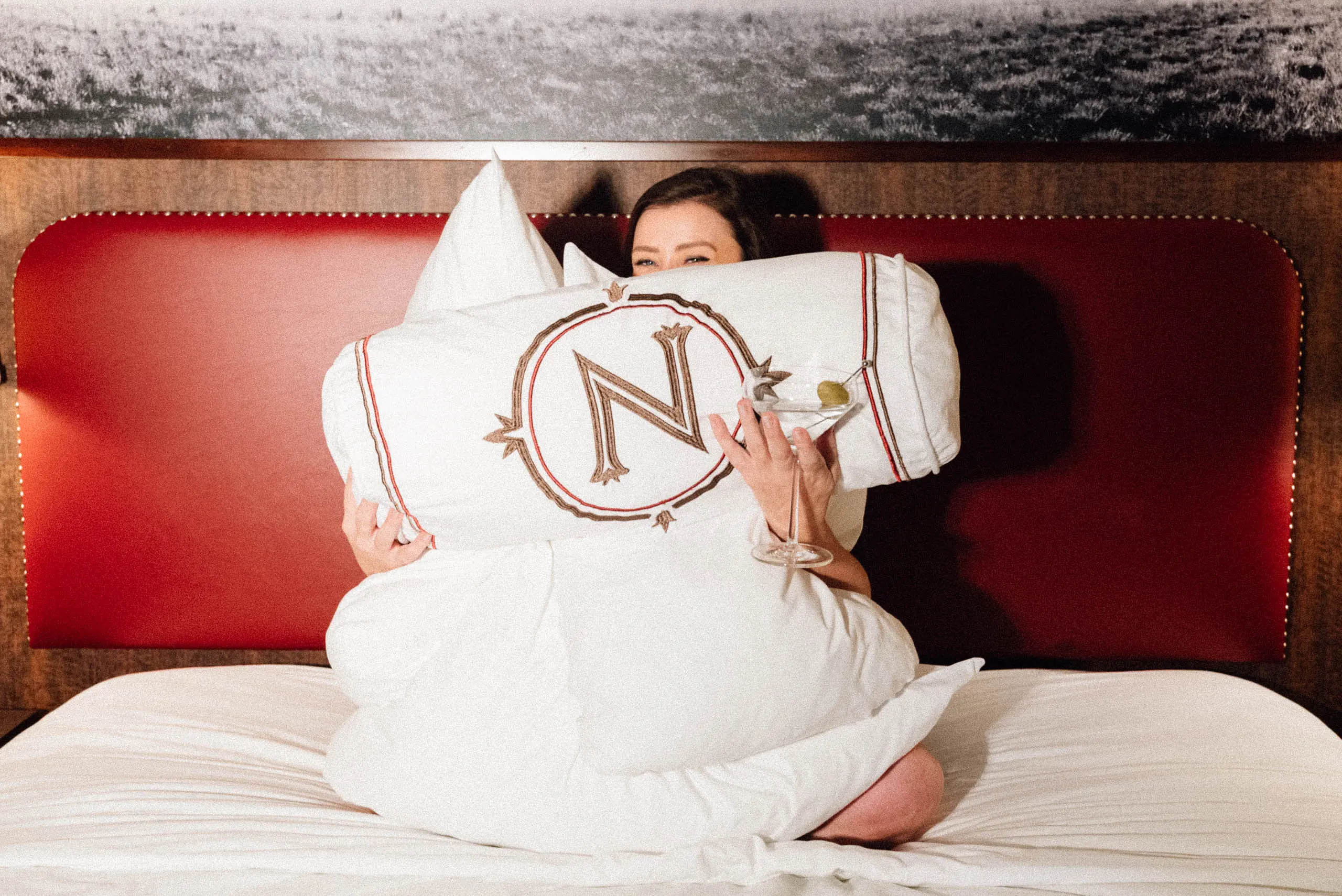 Northern Hotel brand photography, a guest in bed with a martini and a monogrammed pillow