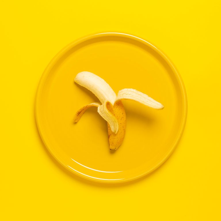 A peeled banana on a yellow plate set against a yellow background, offering vibrant color and texture contrast.