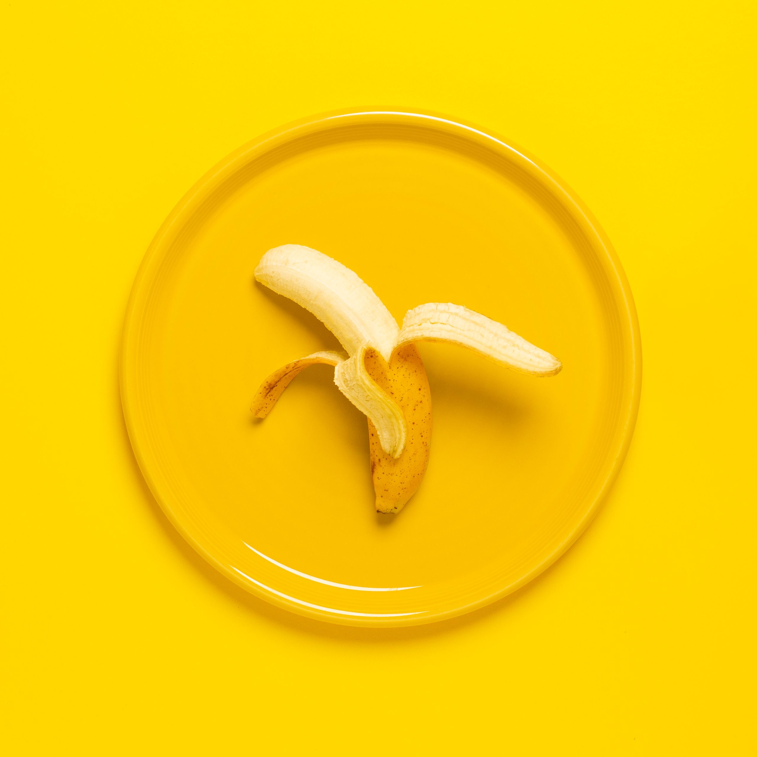 A peeled banana on a yellow plate set against a yellow background, offering vibrant color and texture contrast.