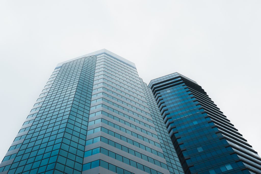 Two glass office towers seen from below, one rising higher than the other
